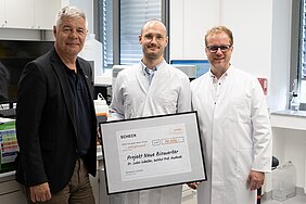 Gunther Schunk übergibt großen Scheck an Lukas Scheller, daneben steht Michael Hudecek. 