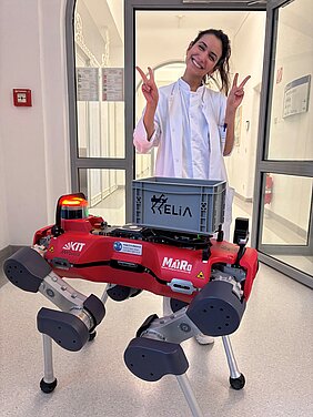 HELIA steht auf dem Flur der Privatambulanz der Hautklinik. Hinter HELIA steht eine fröhliche Mitarbeiterin der Hautklinik.