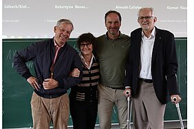 Gewählter Vorstand vor einer grünen Tafel. Prof. Hebestreit stützt sich auf Krücken ab. 