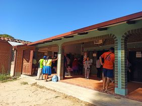 Außenaufname des Krankenhauses in Bolivien, einige Menschen stehen vor der Anmeldung unter einem Vordach.