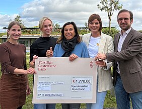 Gabriele Nelkenstock (Hilfe im Kampf gegen Krebs e.V., Mitte), eingerahmt von den Spenderinnen Johanna Oppmann (links) und Rebekka Nöth, außen Antonia Rabe und Prof. Dr. Imad Maatouk, beide von der Medizinischen Klinik II des Uniklinikums Würzburg. Sie halten einen großen Bankcheck, der Fürstlich Castell`sche Bank, mit den Erlösen der Spendenaktion "Rock Race", in Höhe von 1.770,00€, vor sich.