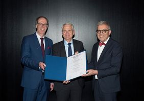 Dirk Heinz (Mitte) bei seiner Ehrenpromotion. Links Universitätspräsident Paul Pauli, rechts Matthias Frosch, Dekan der Medizinischen Fakultät.