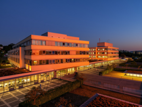 Anlässlich des Welttags der Patientensicherheit erstrahlen das Zentrum für Innere Medizin (ZIM) und das Zentrum für Operative Medizin (ZOM) am Abend des 16. und 17. September 2026 in orangefarbenem Licht. © Katrin Heyer, KI-bearbeitet (orange eingefärbt und Abendstimmung ergänzt)