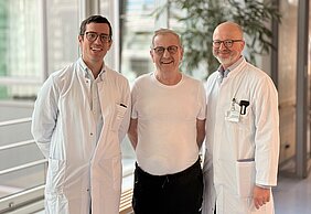 Patient steht zwischen seinen Ärzten in der Magistrale des Zentrums für Operative Medizin. 