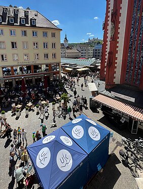 Stand des Uniklinikums mit blauen Pavillons, die mit dem UKW-Logo bedruckt sind, auf dem unteren Markt in der Würzburger Innenstadt