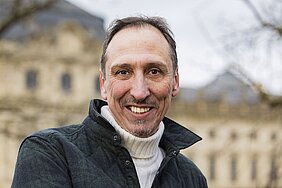 Porträt Prof. Dr. Alexander Meining. Im Hintergrund ist verschwommen ein Gebäude zu sehen. 