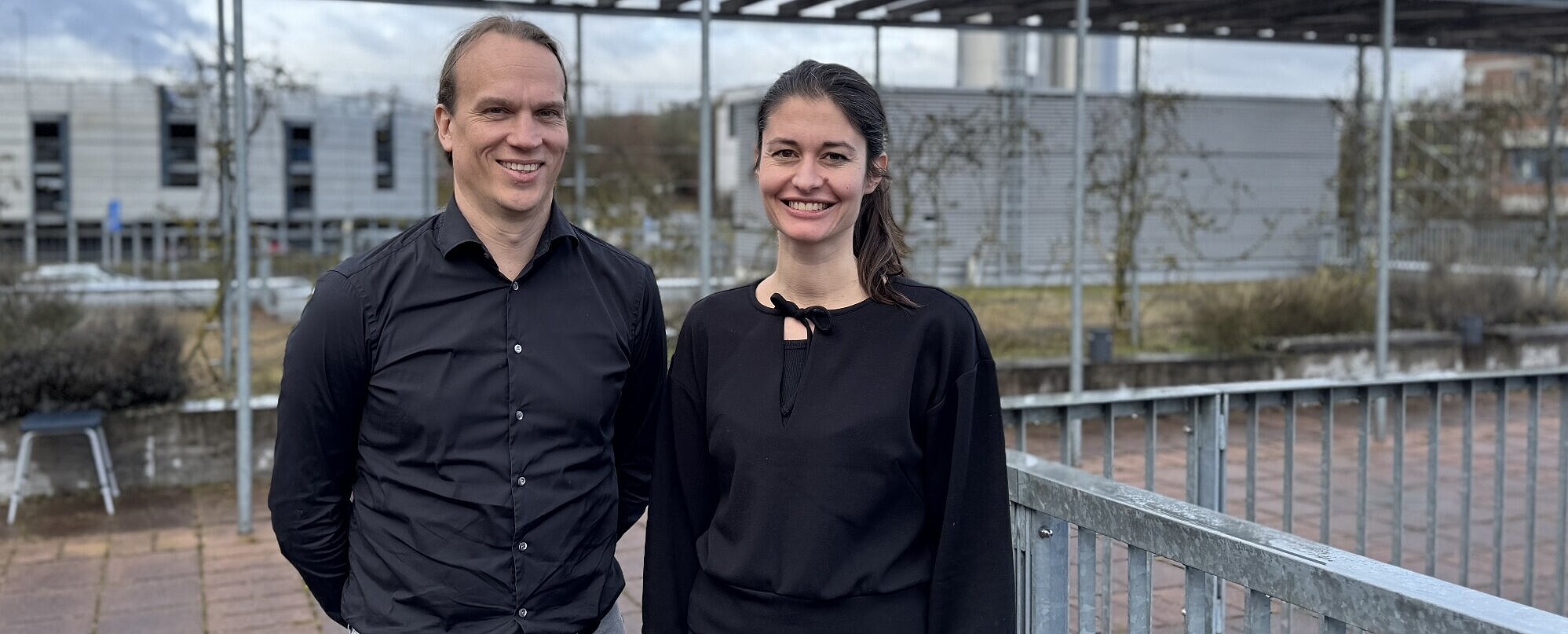 Die beiden Forschenden stehen auf der Terrasse der Medizinischen Klinik II des UKW, im Hintergrund der Helikopter-Landeplatz 