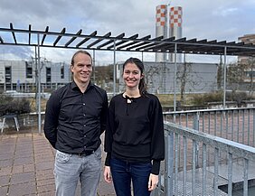 Die beiden Forschenden stehen auf der Terrasse der Medizinischen Klinik II des UKW, im Hintergrund der Helikopter-Landeplatz 