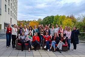 Die Teilnehmerinnen posieren draußen auf einer Hotelterrasse fürs Bild und winken -  vorne sitzen sechs Frauen auf zwei Sofas, dahinter gruppieren sich die anderen Frauen 