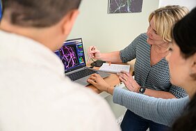 Mateo Andrade Mier, Carmen Villmann und Esra Türker sitzen vor einem Laptop und betrachten ein mikroskopisches Bild, Mateo ist nur von hinten zu sehen. 