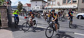 Eine Gruppe Regenbogenfahrer auf ihren Fahrrädern die Grombühlstraße hochradeln und ins Klinikgelände einfahren. 