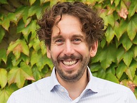 Porträtbild von Martin Reich in hellem Hemd vor einer mit wildem Wein berankten Wand