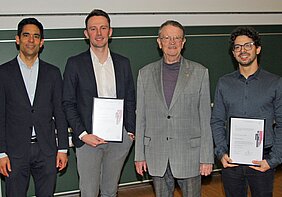 Auf dem Bild stehen vier Herren vor einer grünen Tafel. Zwei der Herren halten in einem Bilderrahmen die Urkunde Hentschel-Preis 2025.