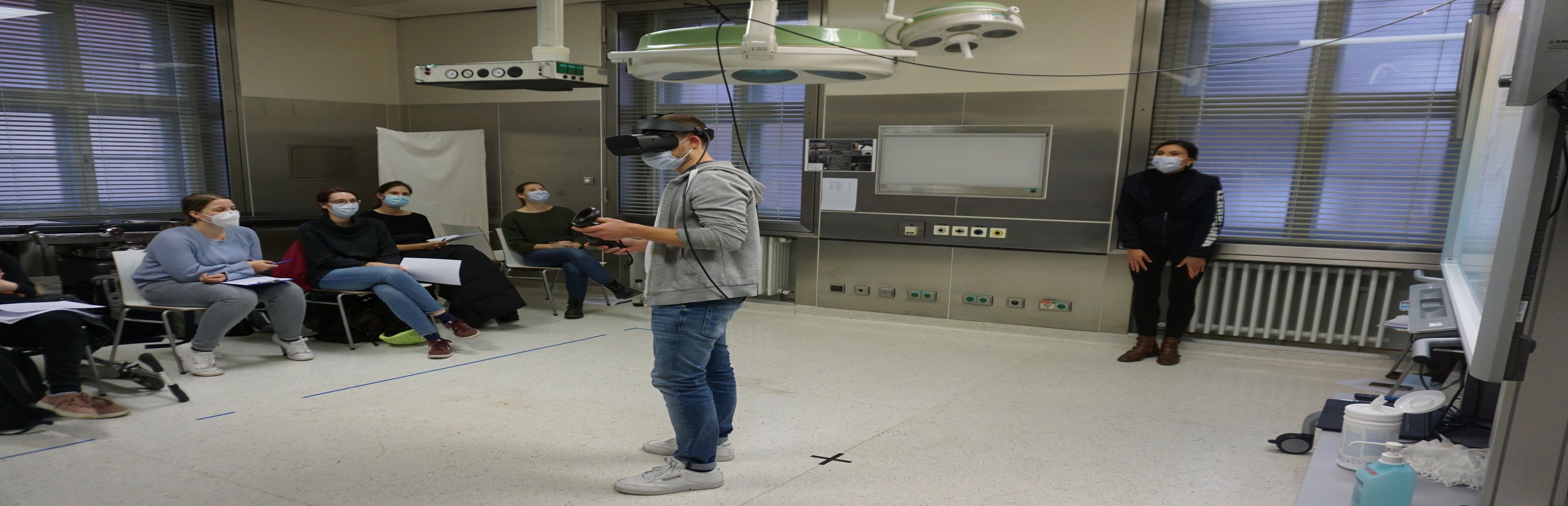 Virtual-Reality-Seminar an der Uni Würzburg mit VR-Brille. Studierende verfolgen den Fall auf einer Leinwand mit.