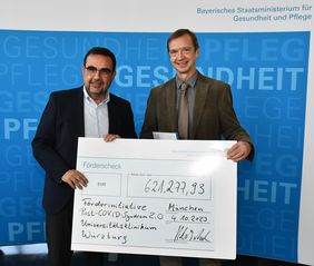 Staatsminister Klaus Holetschek und Rehabilitationswissenschaftler Heiner Vogel mit symbolischem Förderscheck über 621.277,93 Euro .