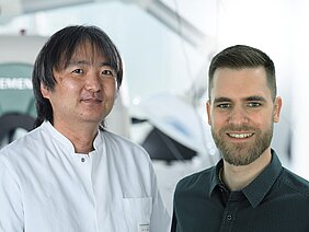 Das bild ist eine Collage und zeigt Takahiro Higuchi im Labor, daneben wurde ein freigestelltes Porträt von Benjamin Heil gesetzt, das sich in die Umgebung einfügt. 