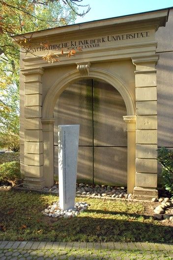 Eingangstor des ersten Klinikbaus von 1893 mit der 2014 aufgestellten Stele zur Erinnerung an die Opfer des Nationalsozialismus (Entwurf: Tilmann Christner, Ausführung: Steinwelten von Josef Hofmann)