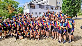 Gruppenfoto der Regenbogenfaher vor der Kinderklinik. Alle Teilnehmer haben ein T-Shirt mit Regenbogen an und teilweise auch mit Regenbogen-Fahnen. 