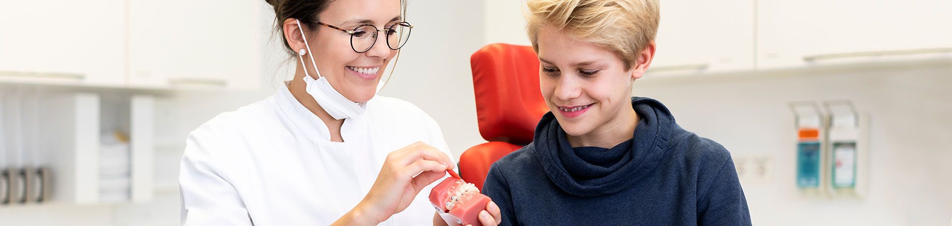 Illustrationsfoto Kieferorthopädie: Ärztin zeigt Patienten die richtige Reinigung der festen Zahnspange an einem Modell