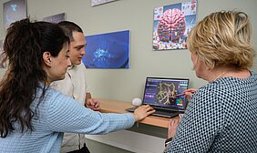 Mateo Andrade Mier, Carmen Villmann und Esra Türker sitzen vor einem Laptop und betrachten ein mikroskopisches Bild, Carmen Villmann ist nur von hinten zu sehen. 