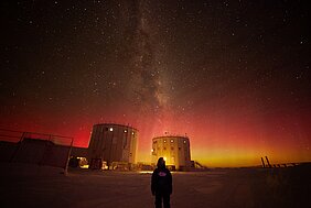 Sternenhimmel über der Concordia-Station - vorn im Bild eine Person, hinten die Station