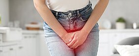 Mensch in Jeans und weißem Shirt  hält Hände gekreuzt über den Schoß
