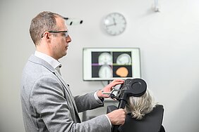 Alexander Soutschek steht im Labor und setzt einer Probandin eine Spule auf den Schädel.