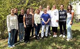 Das Team steht in zwei Reihen bei gutem Wetter unter Bäumen vor der Hautklinik. 