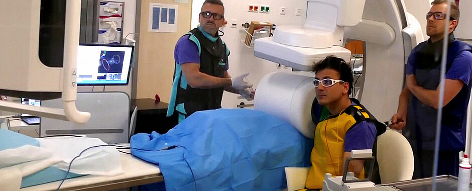Team in der Radiologie - Viktor Hartung hält Arm in MPI-Scanner - alle tragen Bleischürzen und Sicherheitsbrillen