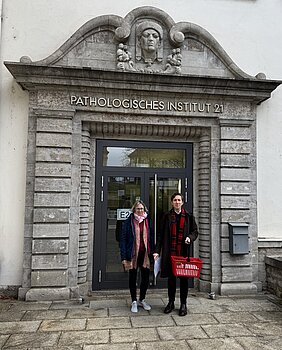 Sebastian Häusner und Eva Baumann stehen mit rotem Körbchen vor der Pathologie 