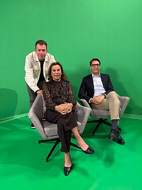 Moderator mit Frau Nelkenstock und Prof. Tim J. von Oertzen im Studio von TV Mainfranken. Hintergrund und Fußboden sind grün.