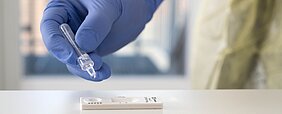 Durchführung eines SARS-CoV-2-Antigenschnelltests. Geraden werden von der Pufferlösung Tropfen auf den Teststreifen gegeben.
