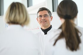 Stefan Störk im weißen Kittel steht vor HI-Nurses, ebenfalls in weißer Arbeitskluft, im Hintergrund ein Flipchart