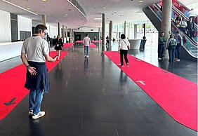 Eine Testperson geht auf dem roten Teppich, eine andere Person steht daneben und misst die Zeit. 