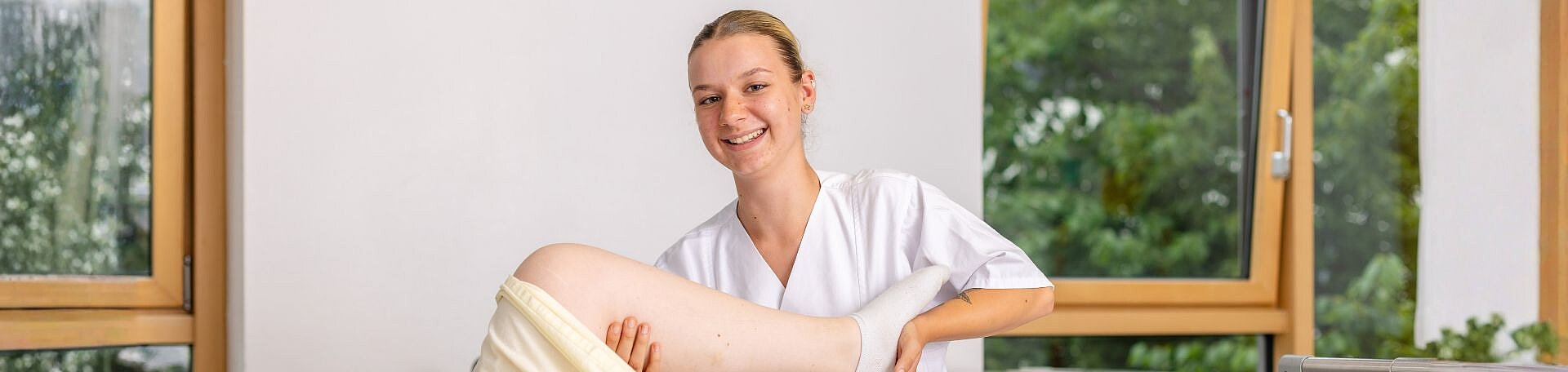 Azubine im Bereich Physiotherapie. Foto: Salih Usta Symbolbild: Azubine aus dem Bereich Physiotherapie am Bett einer Patientin. Die Azubine hält das Bein der Patientin.