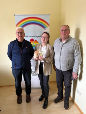 Foto zeigt drei Personen bei der Spendenübergabe, die vor einem Roll-up stehen. In der Mitte hält eine Dame mehrere Geldscheine in der Hand. 