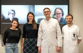 DAs Bild zeigt das Würzburger Team in Person und auf dem Monitor hinter den Personen die zwei Projektpartnerinnen aus Regensburg und München.