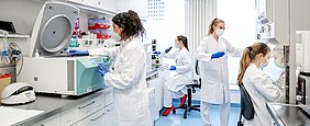 4 Mitarbeiterinnen der Nuklearmedizin am DZHI im Labor an verschiedenen Geräten, alle mit Mundschutz und weißen Kitteln. 