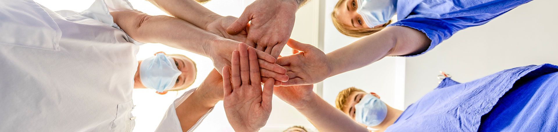 Headerbild: Klinikpersonal legen die Hände zusammen als Zeichen von Teamgedanke