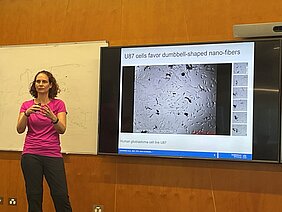 PD Dr. Natascha Schäfer neben einem Bildschirm, auf dem die Powerpoint Präsentation zur ihrem Vortrag läuft