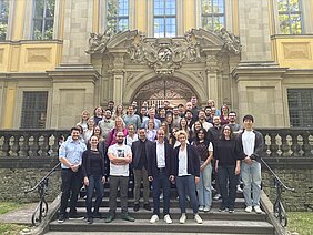 Gruppenfoto der 50 Teilnehmenden beim Retreat des Lehrstuhls für zelluläre Immuntherpie. Die Gruppe steht hintereinander aufgereiht auf einer Treppe vor einem steinernen Gebäude.