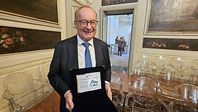 Hermann Einsele hält Urkunde in den Händen und strahlt in die Kamera 