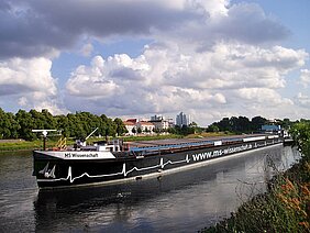 Das Boot mit schwarzem Rumpf fährt auf einem Fluss durch eine grüne Landschaft 