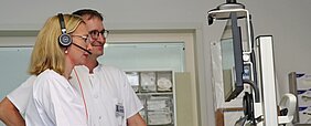 Zwei Mitarbeitende der Anästhesiologie stehen an einem Tele-Intensivmedizin-Wagen vorm Monitor 