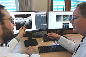 Dr. Andreas Berlin (links) und Prof. Dr. Jost Hillenkamp von der Würzburger Universitäts-Augenklinik diskutieren die vom Programm Fluid Monitor (linker Bildschirm) angebotenen Diagnose-Informationen zur feuchten altersbedingten Makuladegeneration.  Regina Vornberger / UKW