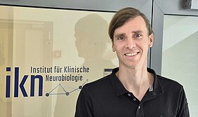 Dominik Groos vor einer Glastür mit der Beschriftung ikn Institut für Klinische Neurobiologie
