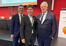 Die drei Autoren der Studie stehen in Anzügen vor der Bühne des HFA Kongresses.