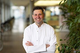 Der Mediziner steht in weißem Kittel mit verschränkten Armen im Flur des Zentrums für Operative Medizin 