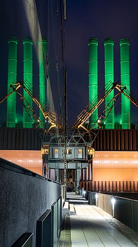 Kamine des Würzburger Heizkraftwerks am Tag der Seltenen Erkrankungen, die farbig beleuchtet sind. 