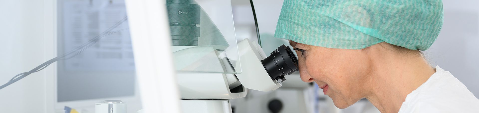 Labor-Mitarbeiterin blickt in ein Mikroskop